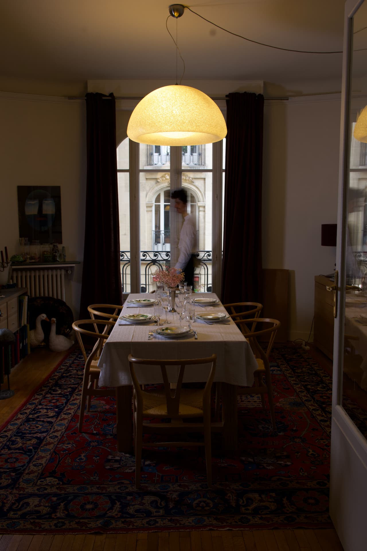 Table dressée sous la lampe, le chef passe près de la fenêtre