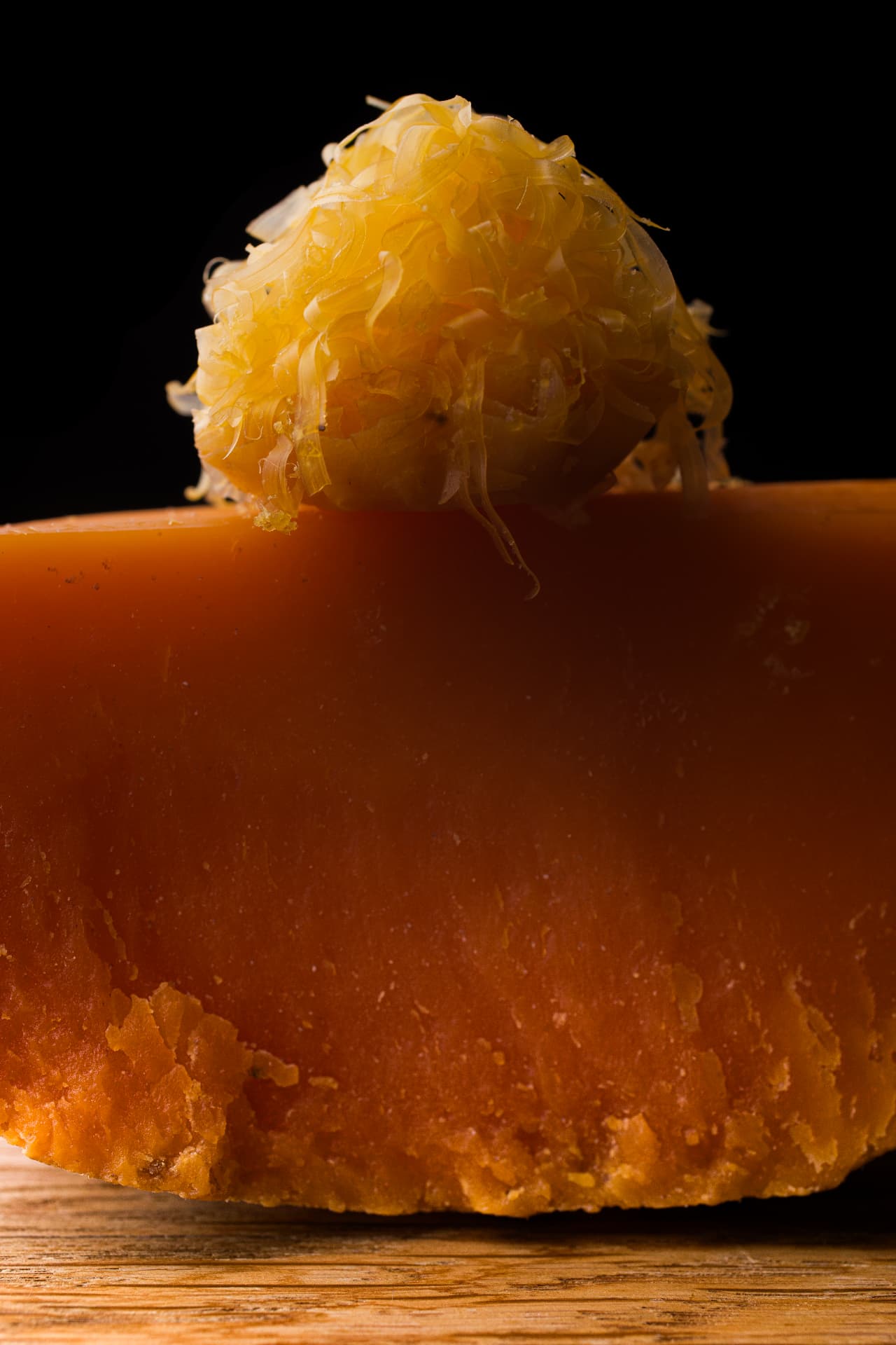 Gros plan sur un fromage ambré coiffé d'un éclat d'agrumes confits, fond noir