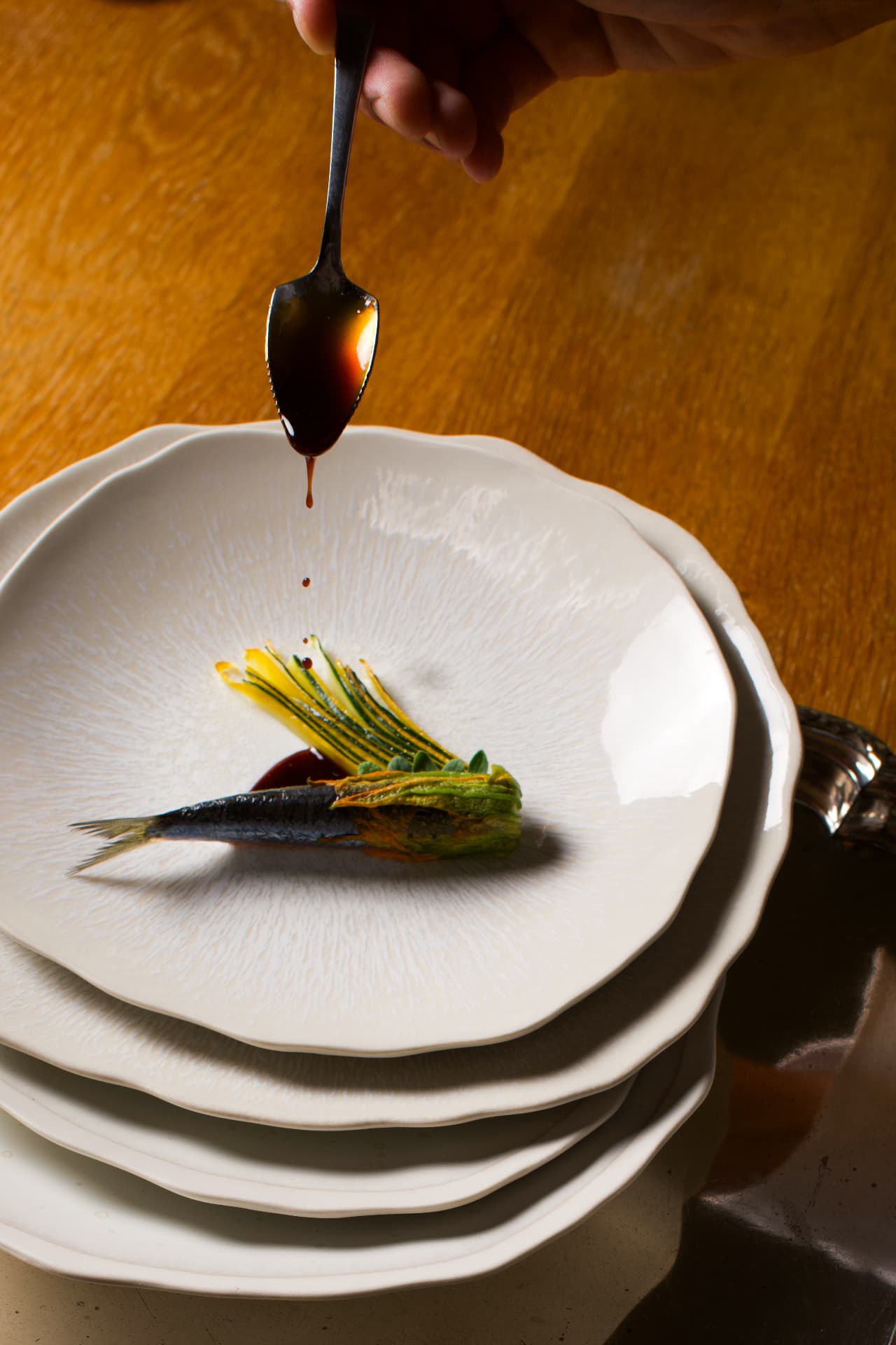 Sardine et fleur de courgette, sauce versée à la cuillère sur une assiette blanche