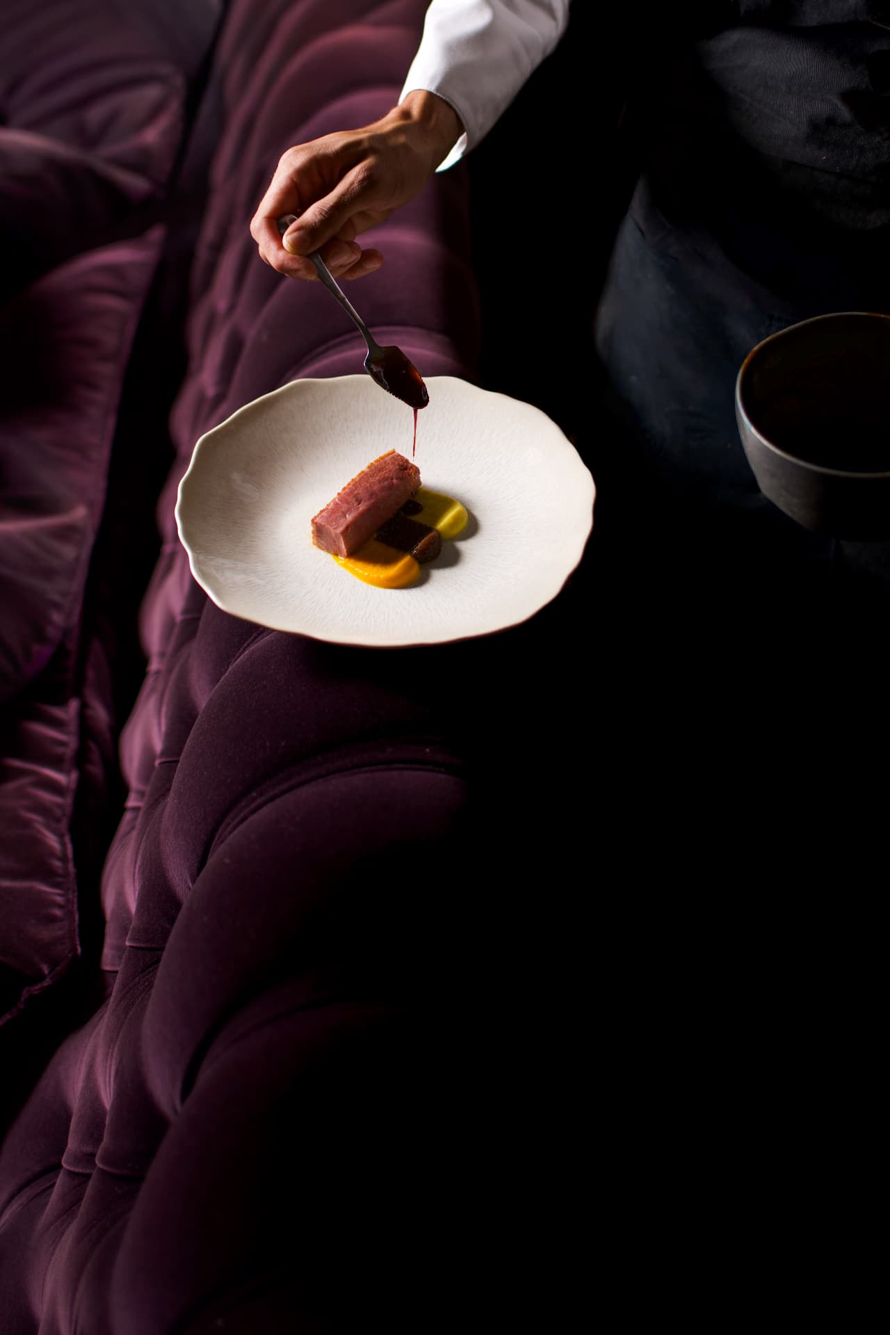Sauce versée sur un pavé de viande rose posé sur un canapé violet